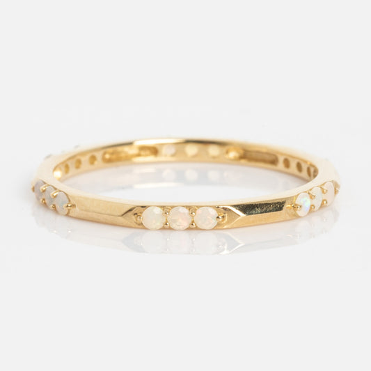 The Solid Gold Beveled Opal Stacking Ring features small round opal stones evenly spaced around its thin gold band, shown on a plain white background.