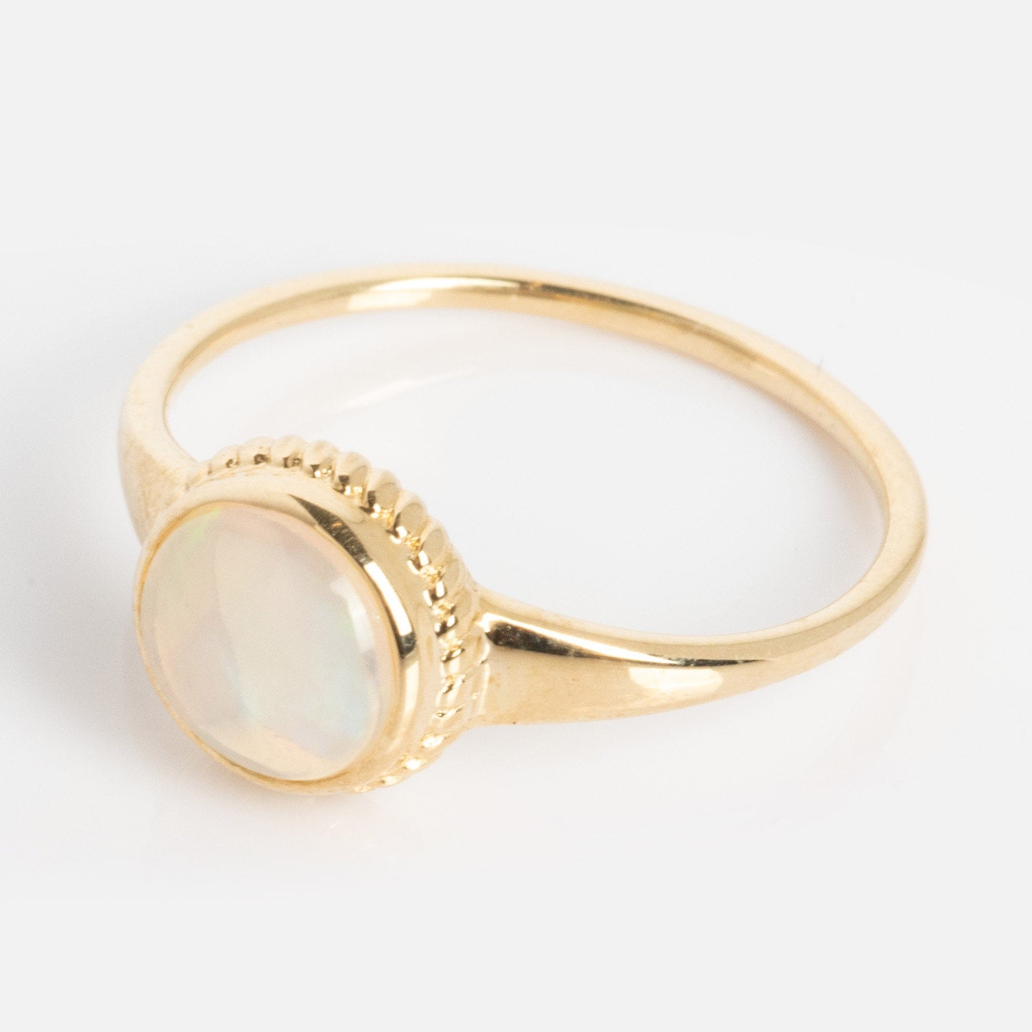 The Solid Gold Textured Opal Signet Ring features a round opal gemstone set in an elegant textured gold band, shown against a white background.