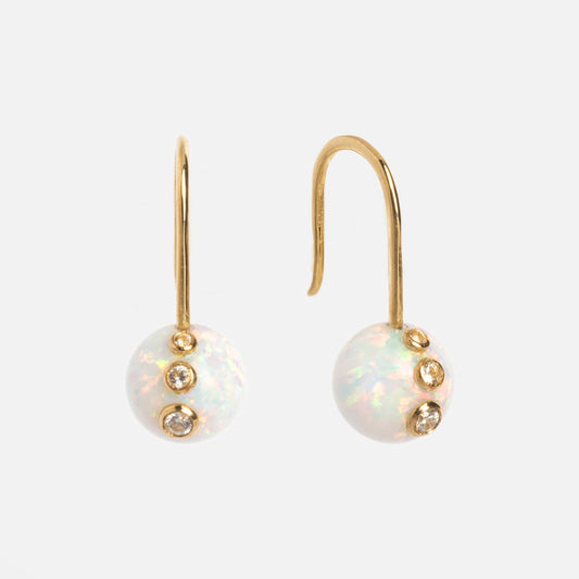 The Solid Gold Floating Opal Gem Drop Earrings feature round opals on gold hooks, each opal accented by three vertically aligned bezel-set diamonds, displayed against a plain white background.