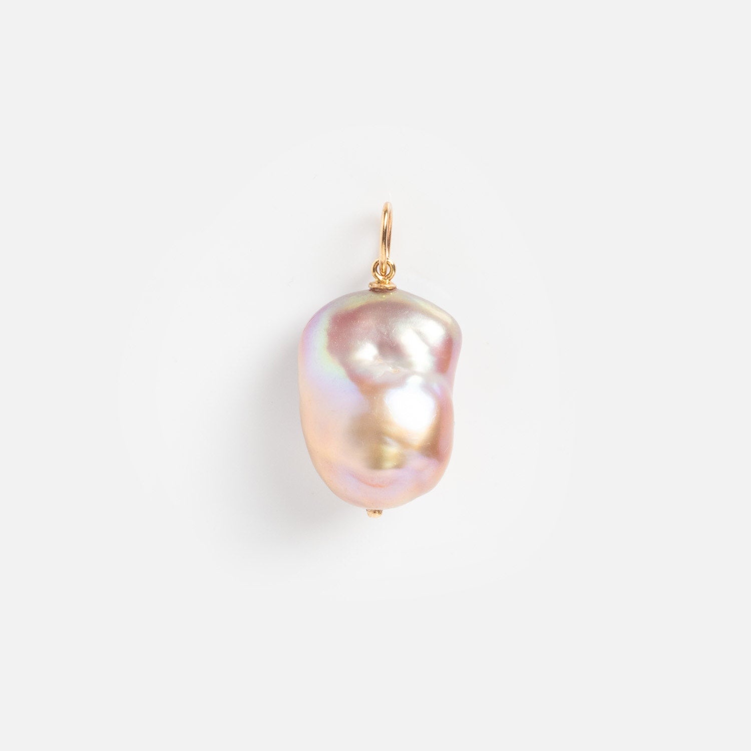 The Solid Gold Statement Charm features a single, irregularly shaped baroque pearl pendant with a gold loop, resting on a white background and showing pink, gold, and lavender iridescence—ideal for lovers of unique jewelry.
