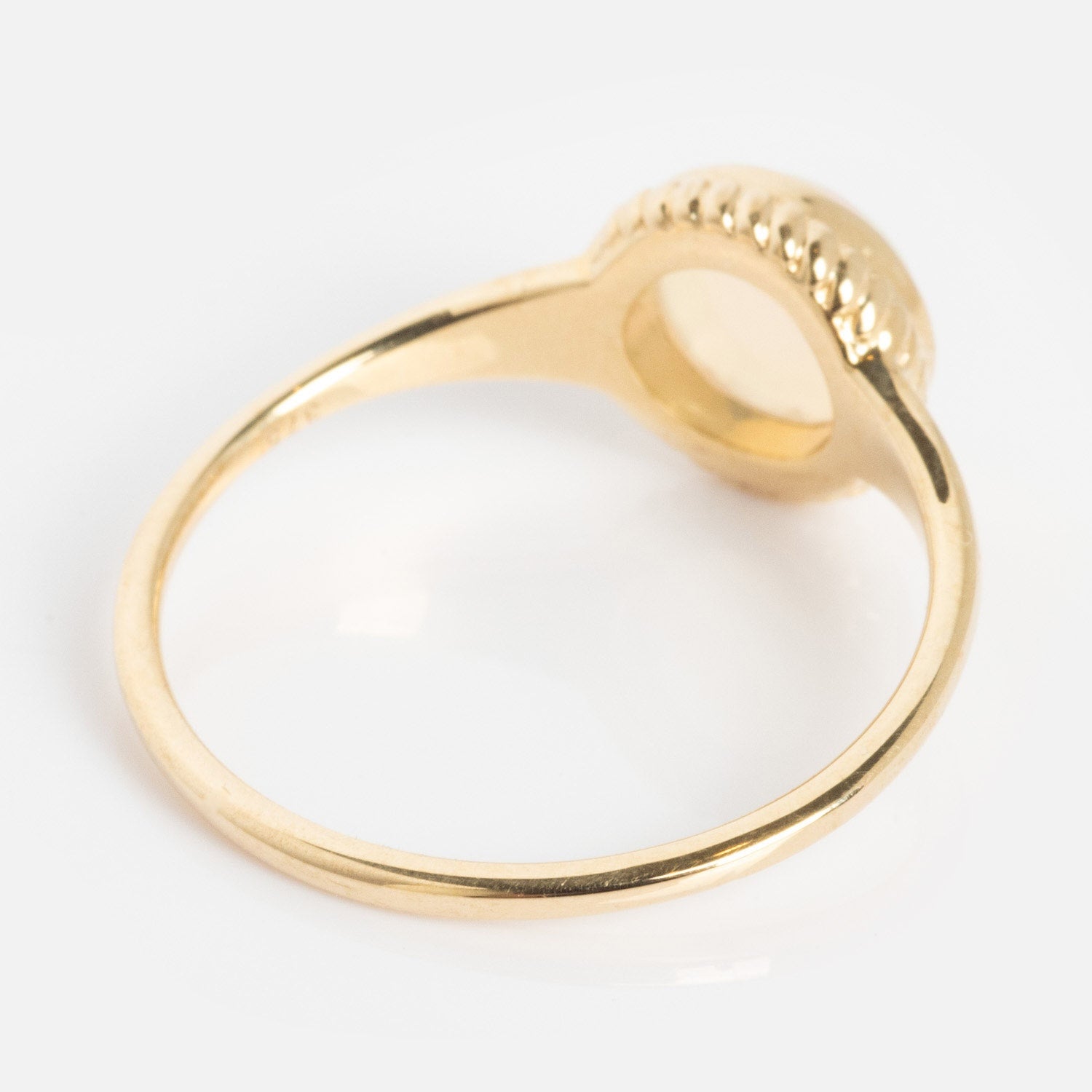 A Solid Gold Textured Opal Signet Ring with a thin band and a round, raised bezel setting is shown from an angle that highlights the underside of the setting against a plain white background.