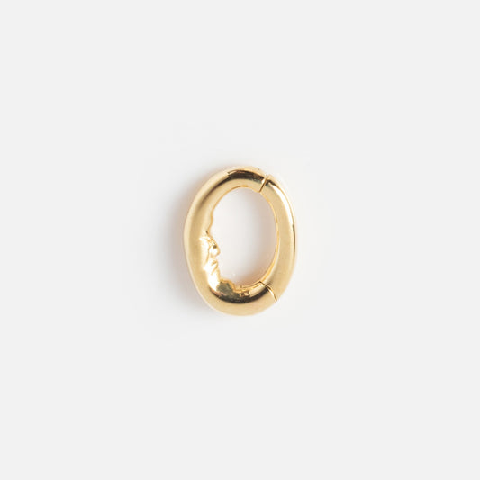 The Solid Gold Ring Clip is a small, oval-shaped gold accessory with an embossed human face on one side, ideal for pairing with your favorite ring stack. Shown against a plain white background.