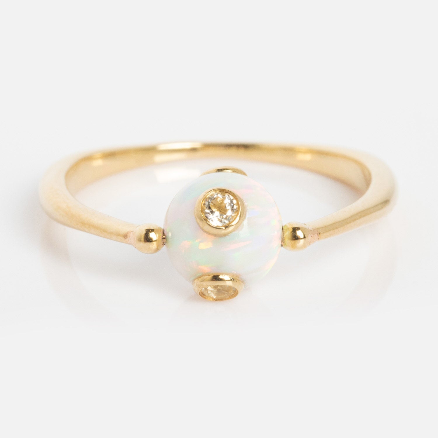 The Solid Gold Gem Drop Opal Spinner Ring features a delicate gold band with a central round opal and a small diamond accent above, beautifully displayed on a light background.