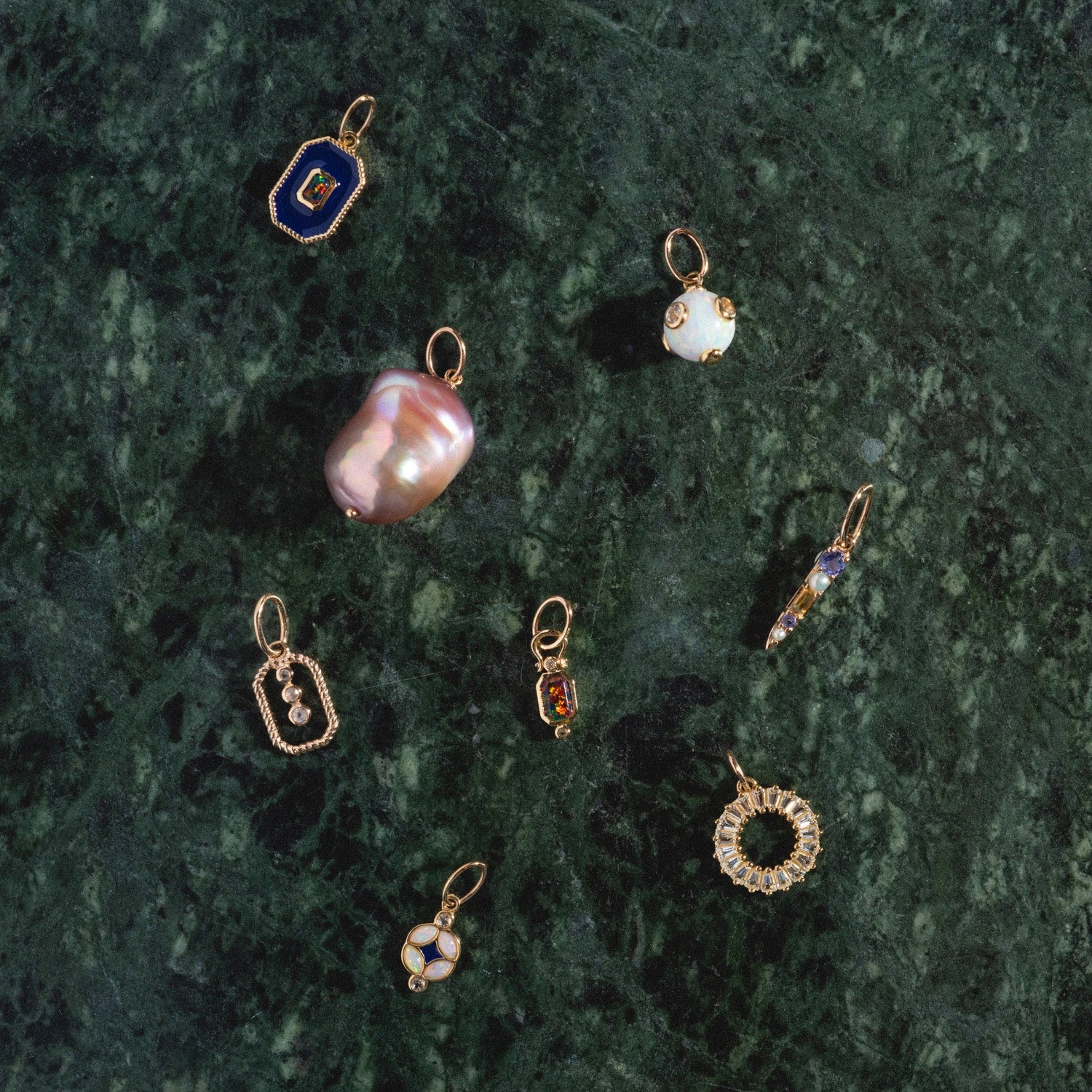 The Solid Gold Statement Charm pendant, a Local Eclectic exclusive, is displayed on a dark green marble surface alongside other pearl and floral designs.