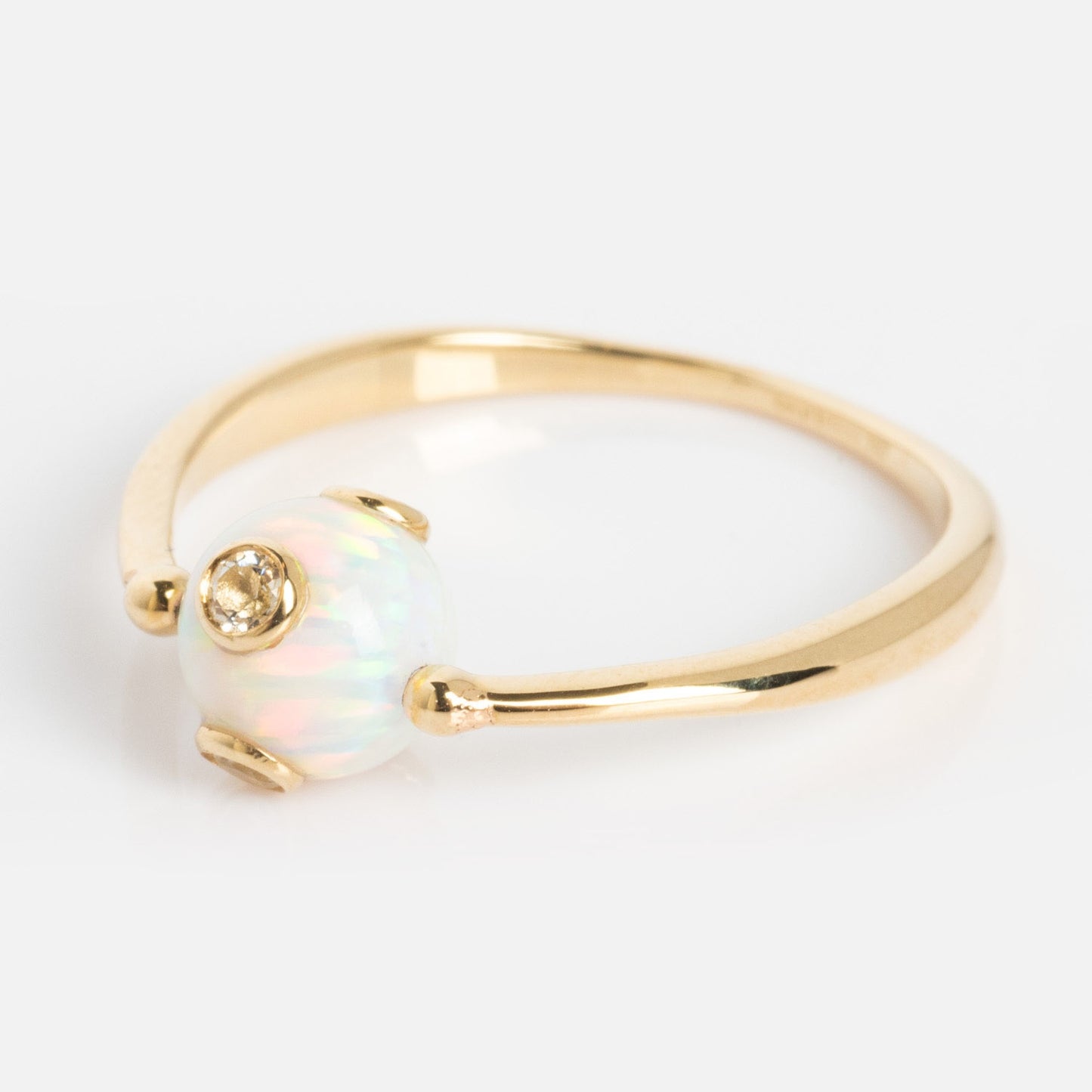 The Solid Gold Gem Drop Opal Spinner Ring features a delicate gold band with a round, iridescent opal bead accented by a small diamond set into the opal, displayed against a plain white background.