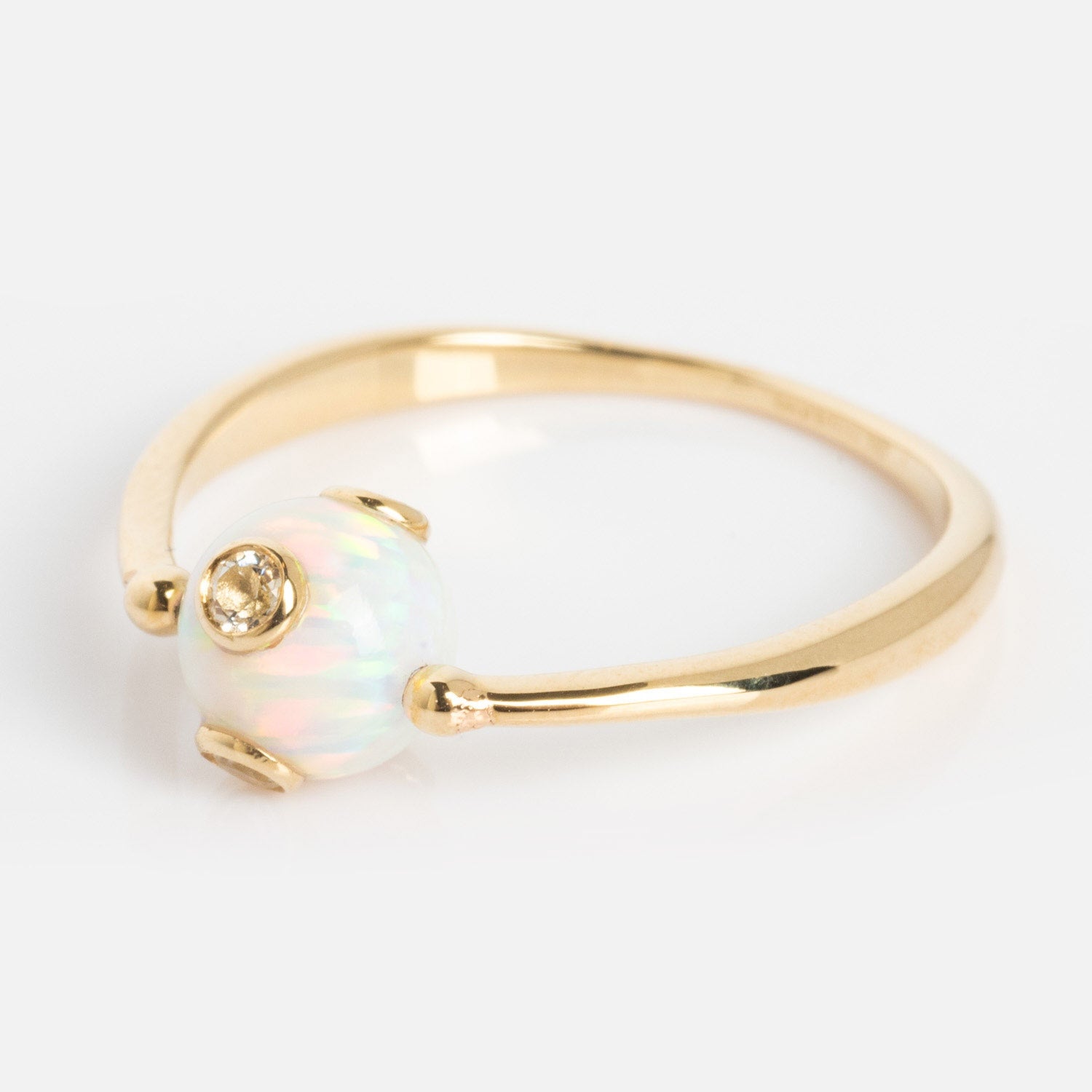 The Solid Gold Gem Drop Opal Spinner Ring features a delicate gold band with a round, iridescent opal bead accented by a small diamond set into the opal, displayed against a plain white background.