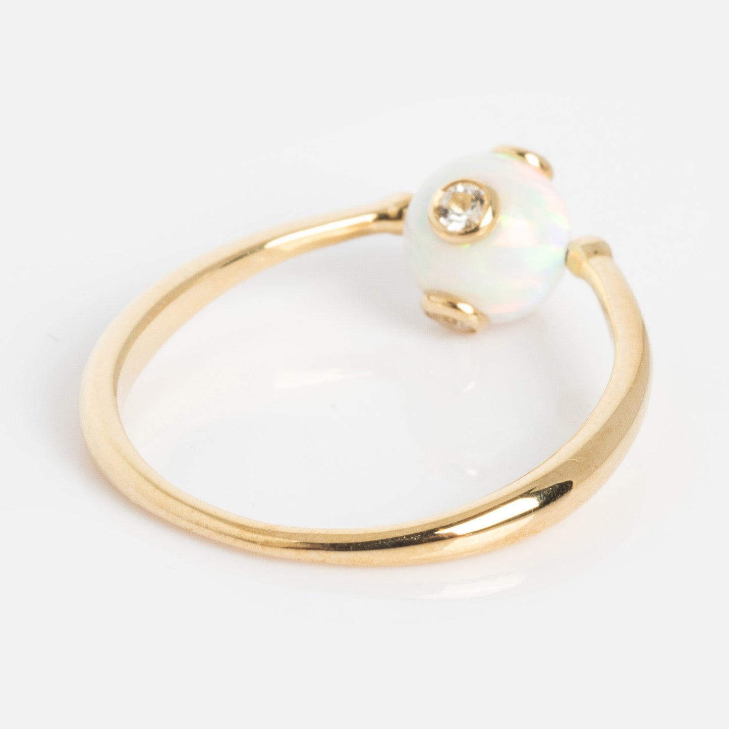 The Solid Gold Gem Drop Opal Spinner Ring features a round opal gemstone accented by a central sparkling diamond, elegantly displayed on a plain white background.
