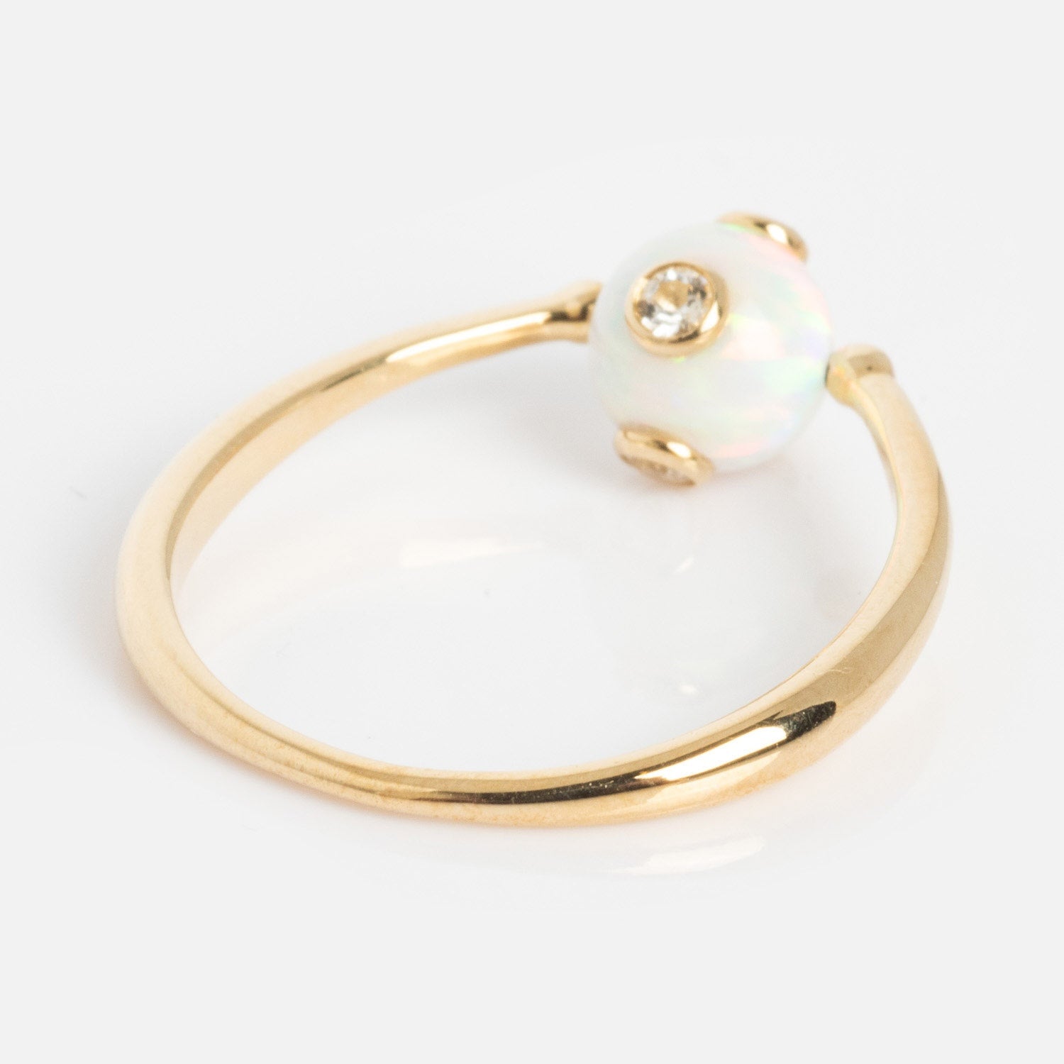 The Solid Gold Gem Drop Opal Spinner Ring features a round opal gemstone accented by a central sparkling diamond, elegantly displayed on a plain white background.