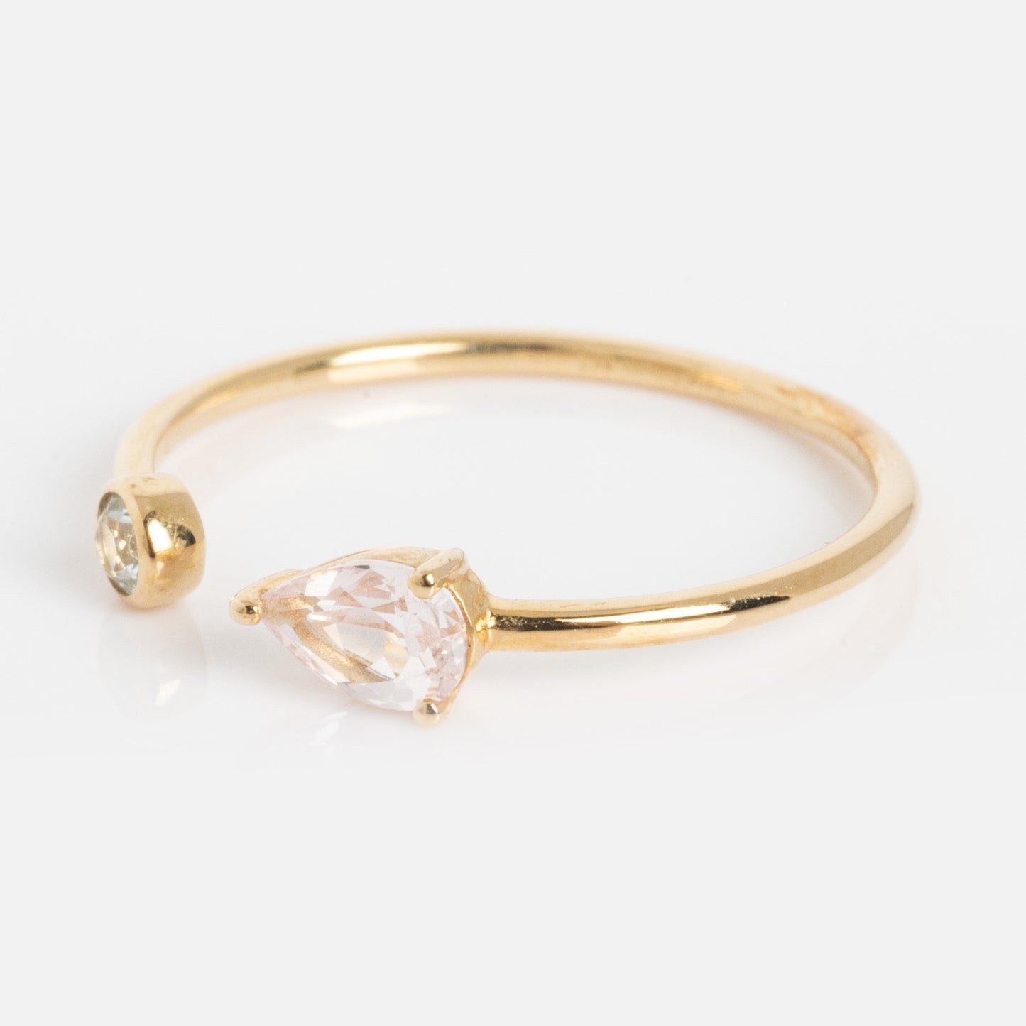 A slim solid gold ring with a pear-shaped sapphire on one end and a small round aquamarine on the other, shown on a white background.