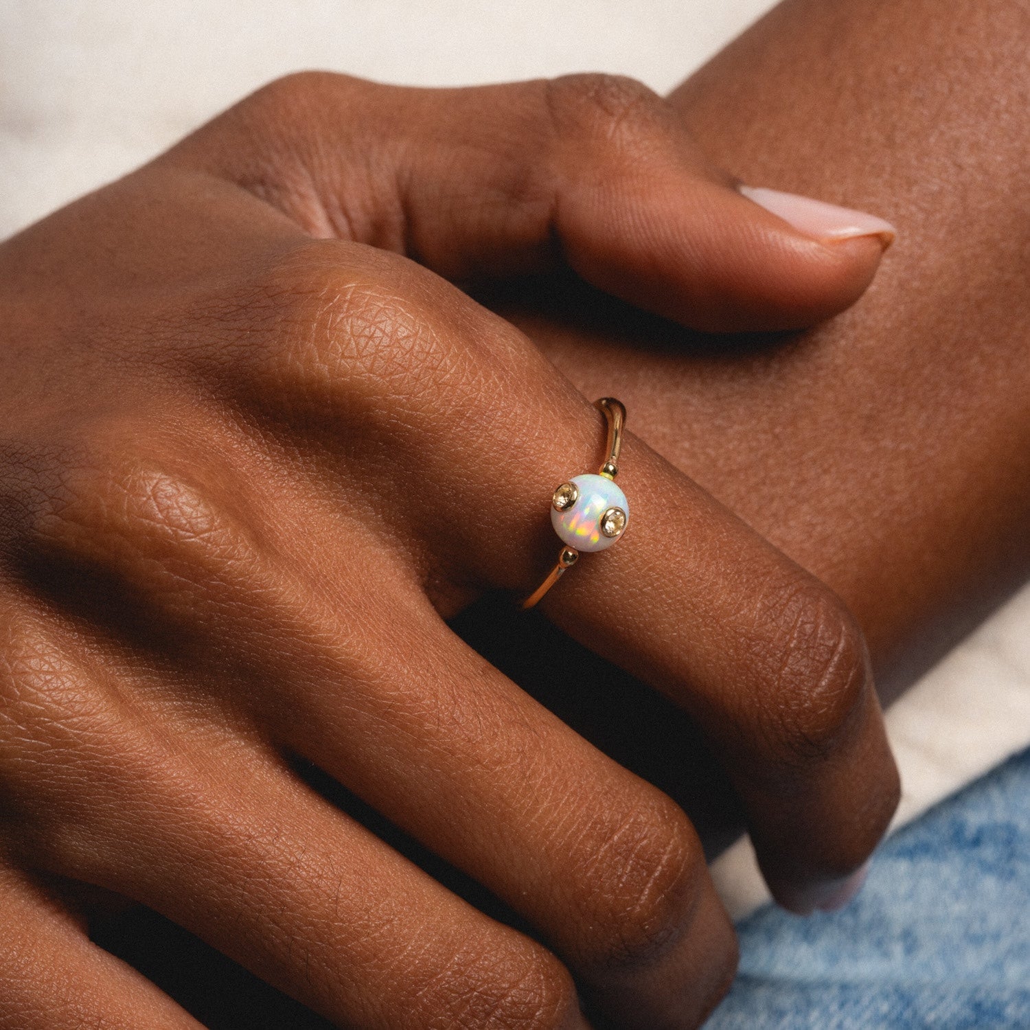 A close-up of a hand wearing the Solid Gold Gem Drop Opal Spinner Ring, featuring a round opal and two small gold accents, resting gently on another hand.