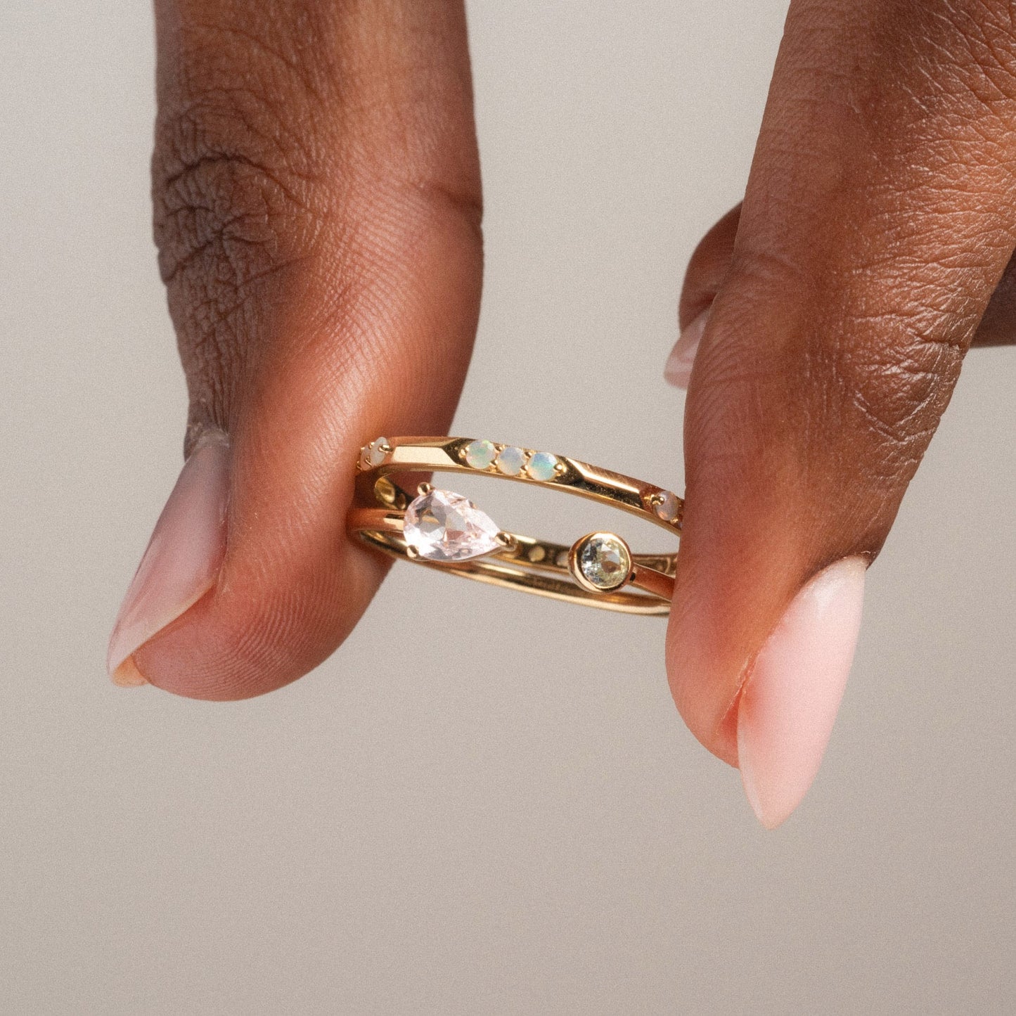 A hand with pale pink nails holds the Solid Gold Sapphire and Aquamarine Open Front Ring, a delicate gold piece adorned with sparkling sapphire and aquamarine gemstones set along its open band.