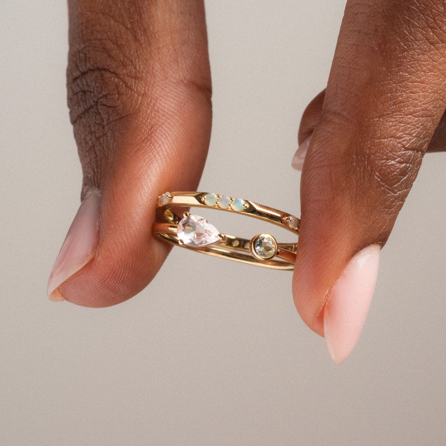 A hand with pale pink nails holds the Solid Gold Sapphire and Aquamarine Open Front Ring, a delicate gold piece adorned with sparkling sapphire and aquamarine gemstones set along its open band.