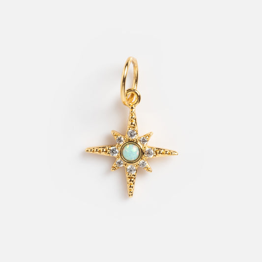 Charms by Jurate JLA: An eight-point gold star pendant with simulated diamonds and a central opal-like gem, hanging from a yellow gold plated loop, shown on a plain white background.
