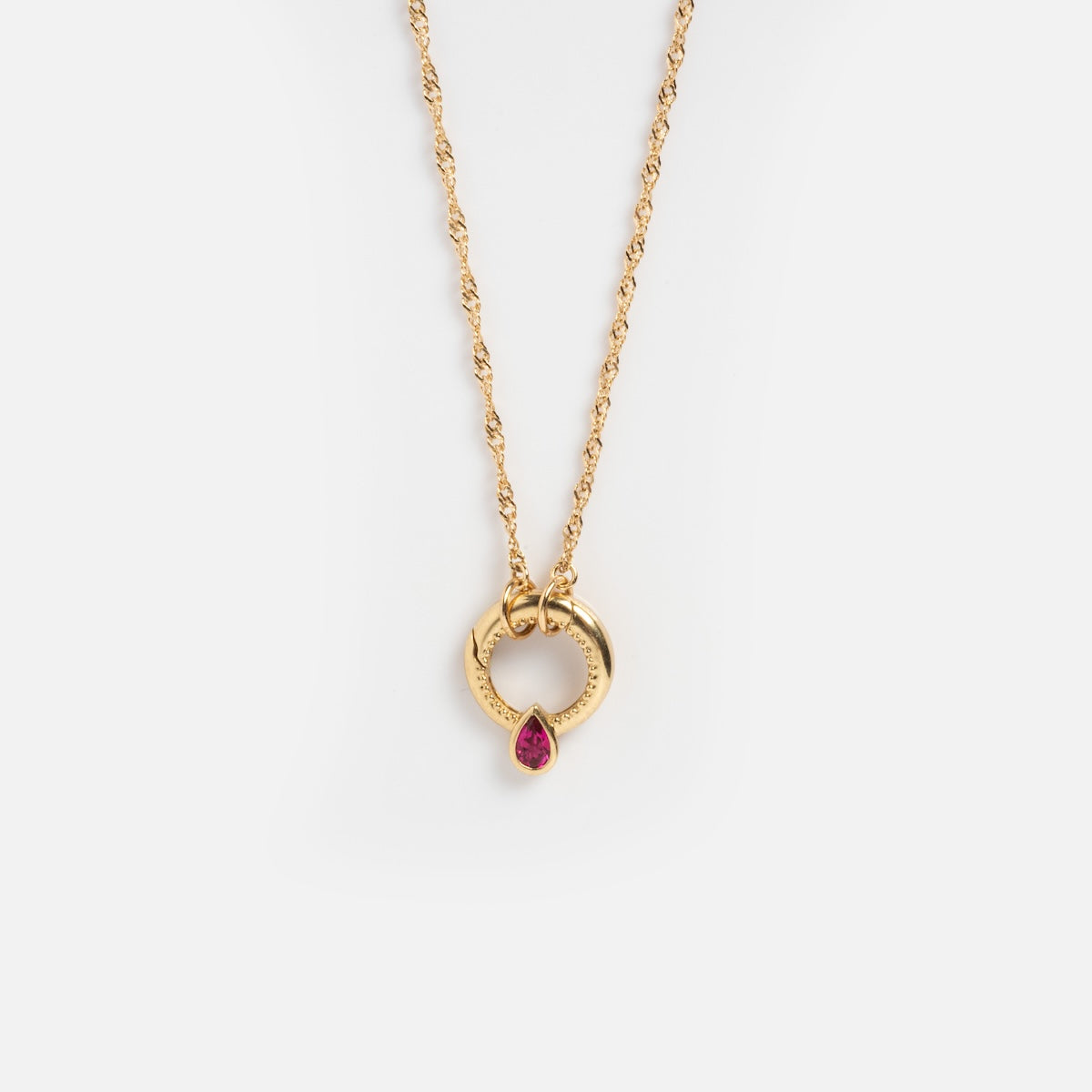 The Solid Gold Perfect Start Charm Holder Necklace features a gold chain with a circular pendant and a small teardrop-shaped pink gemstone inside, shown on a white background.
