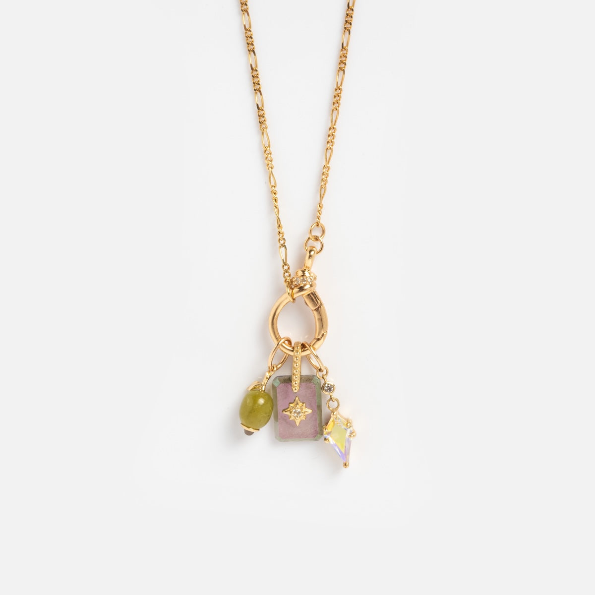 The Solid Gold Figaro Charm Holder Necklace features a gold chain with three charms—a green stone, a rectangular pink pendant with a star design, and an iridescent crystal-shaped charm—suspended from a circular gold ring.