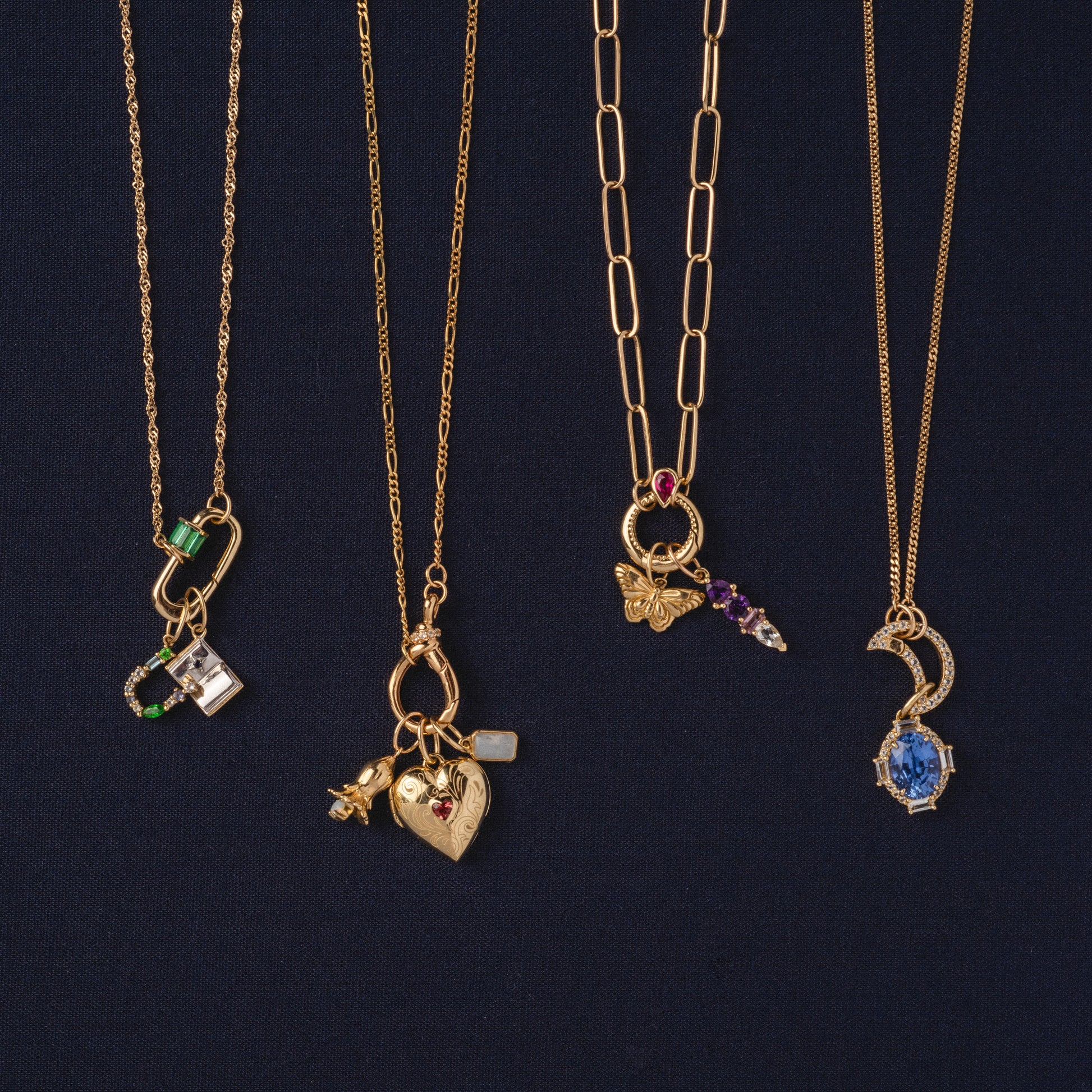 Four Solid Gold Perfect Start Charm Holder Necklaces are displayed against a dark background, each with unique pendants: a locket, various charms, a butterfly, colorful gemstones, and an ornate blue stone.