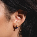 Close-up of a person with dark hair wearing Solid Gold 2025 September Capsule Classic Blue Sapphire Stud Earrings—crafted in 9k yellow gold, set with white topaz and a dangling teardrop blue sapphire, beautifully detailed against a softly lit background.