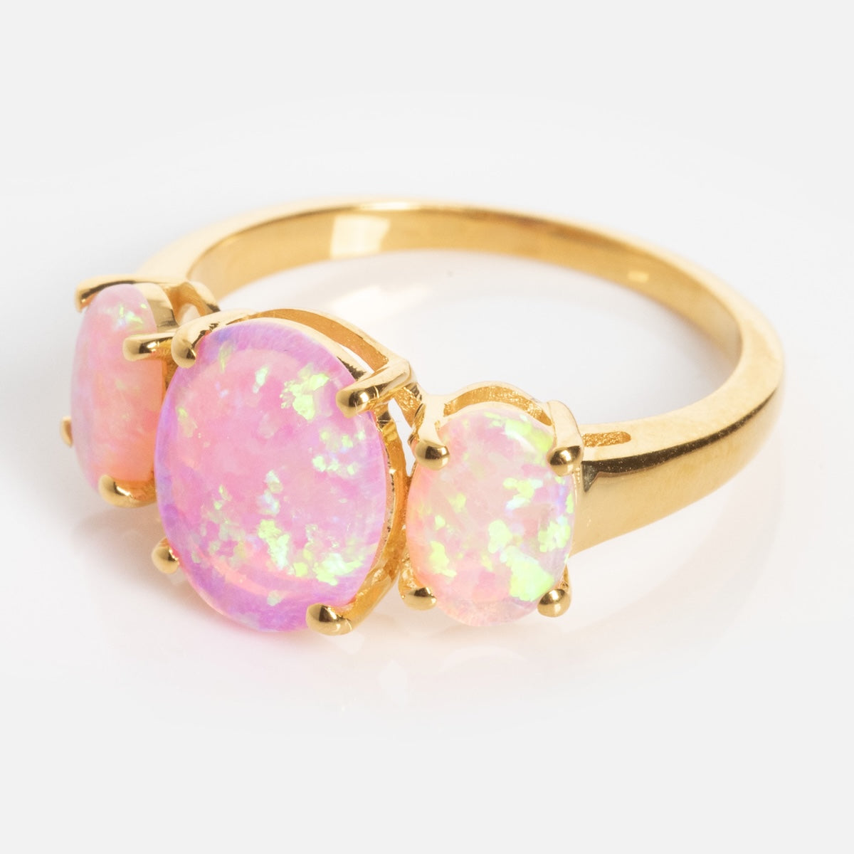 The Pink Opal Gum Drop Ring features three oval pink opal gemstones with iridescent flashes, prong-set in gold and displayed against a white background.