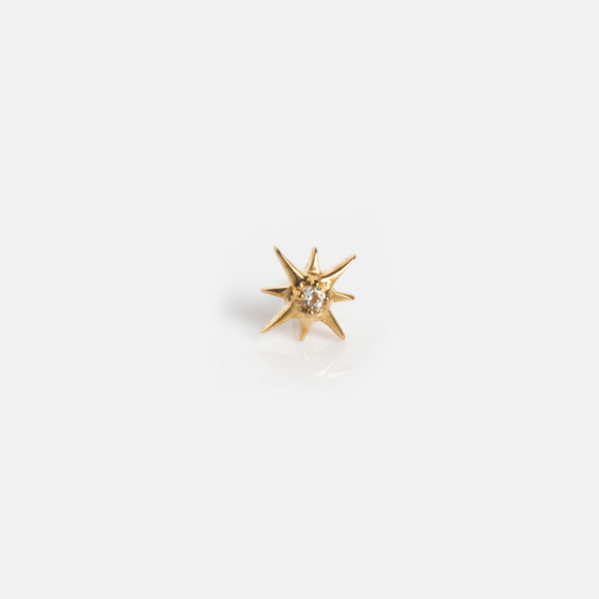 The Solid Gold Starburst Flat Back Stud features a small, star-shaped design with pointed rays and a clear central gemstone, displayed on a plain white background.