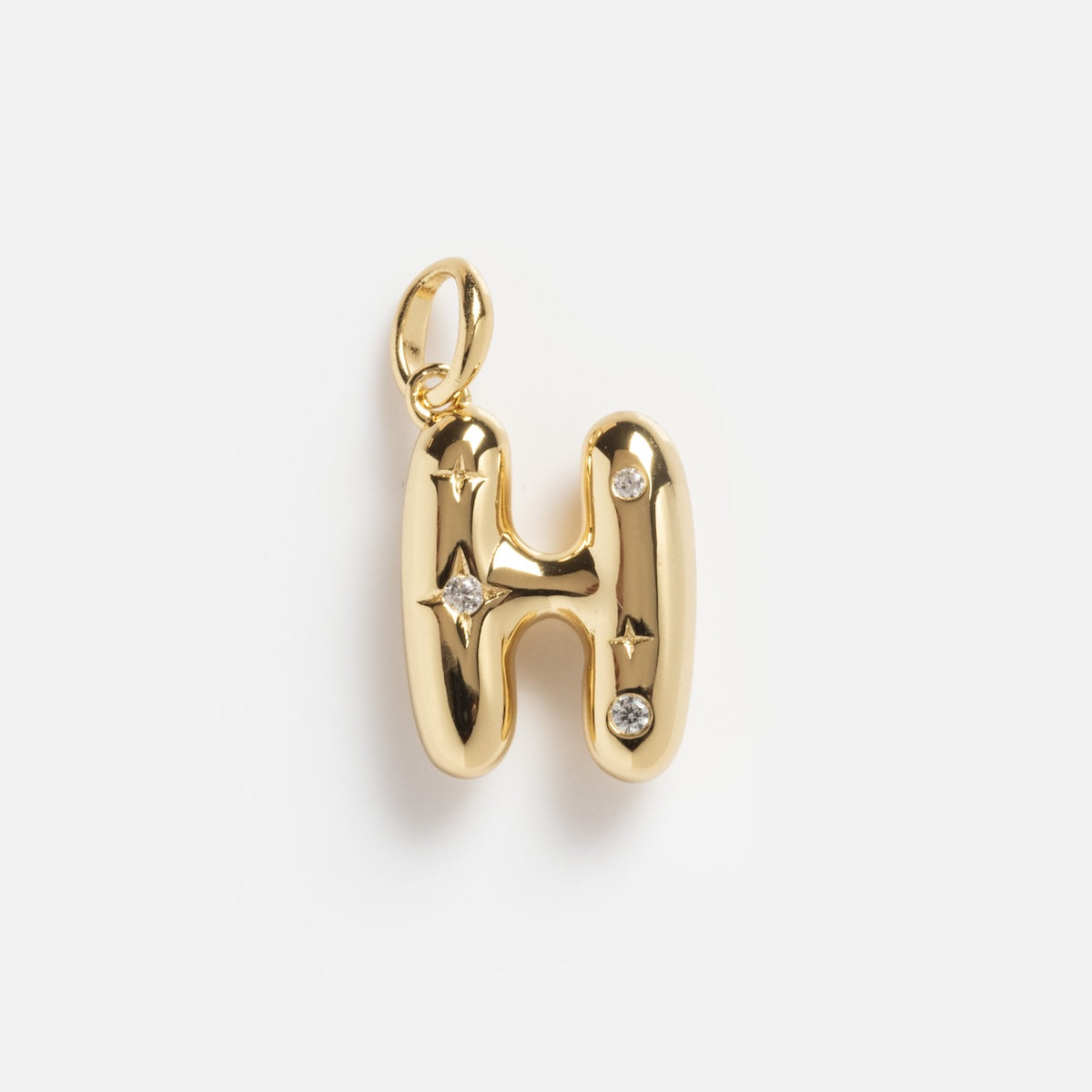 The Star Crossed Celestial Bubble Letter Charm is a gold pendant shaped like the letter H, featuring two small gemstones and star engravings, shown on a plain white background.