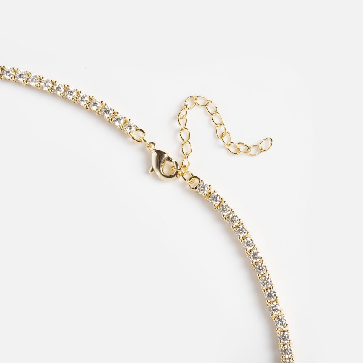 Close-up of the Queen of Hearts Tennis Necklace, a gold chain featuring clear, round gemstones and an adjustable extender, displayed on a white background.
