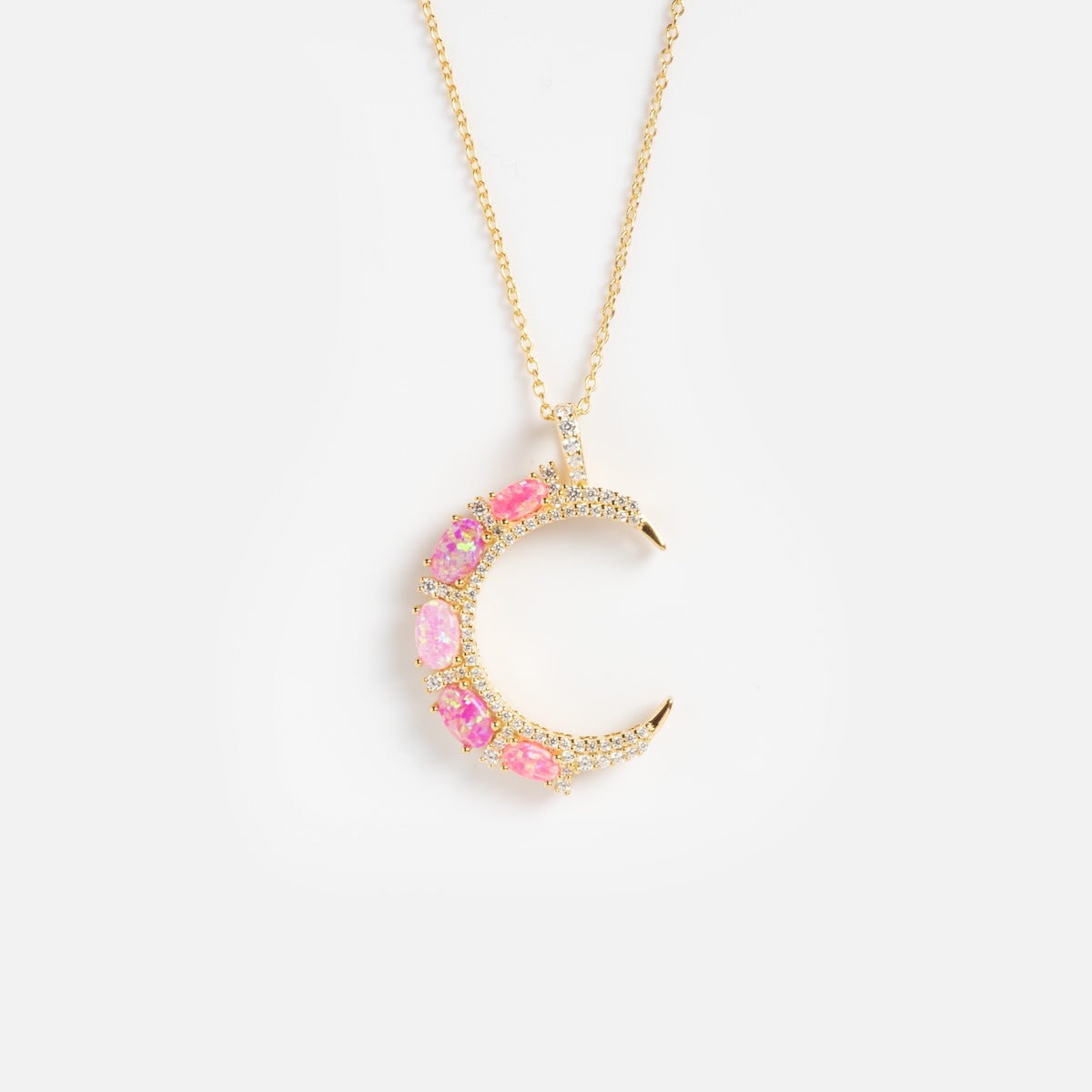 The Pink Opal Crescent Moon Pendant features pink and iridescent gemstones set in a gold crescent moon, elegantly hung on a fine gold chain and shown against a plain white background.