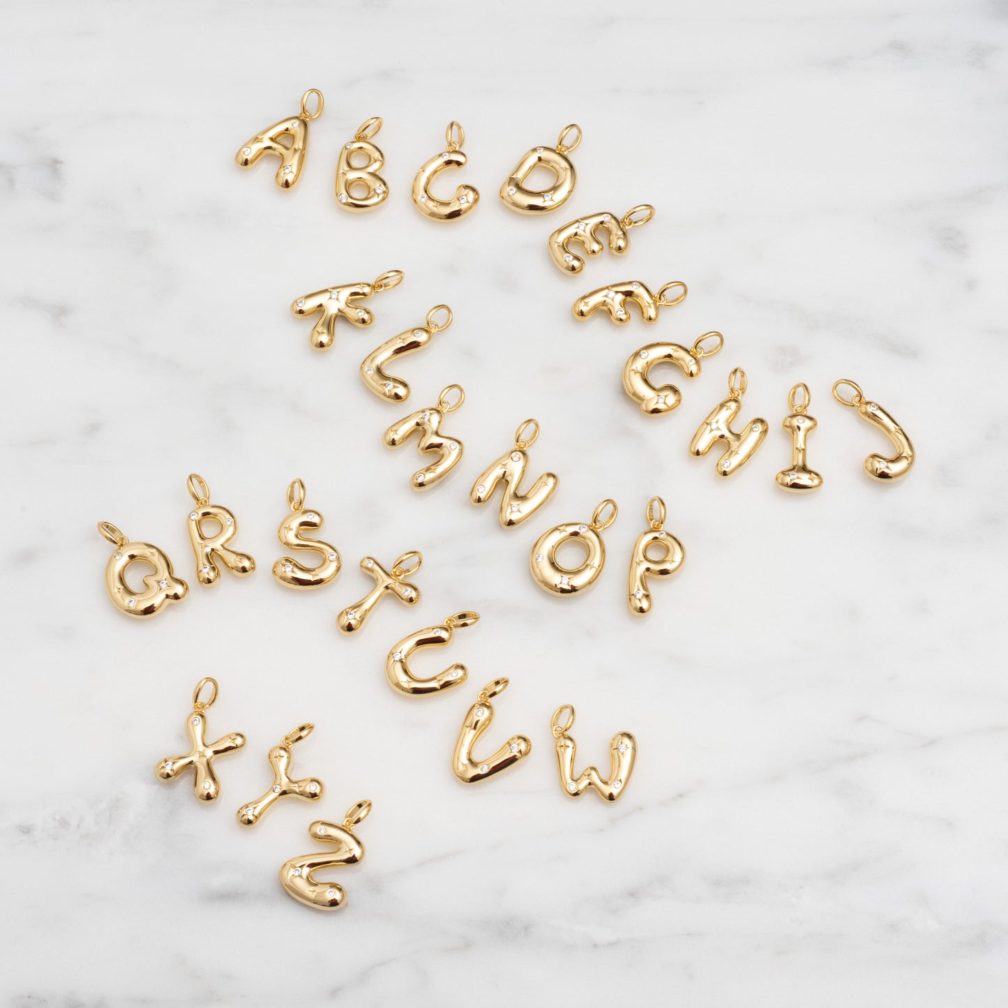 Star Crossed Celestial Bubble Letter Charms arranged on white marble, each charm displays a playful, rounded bubble font featuring letters A to Z.