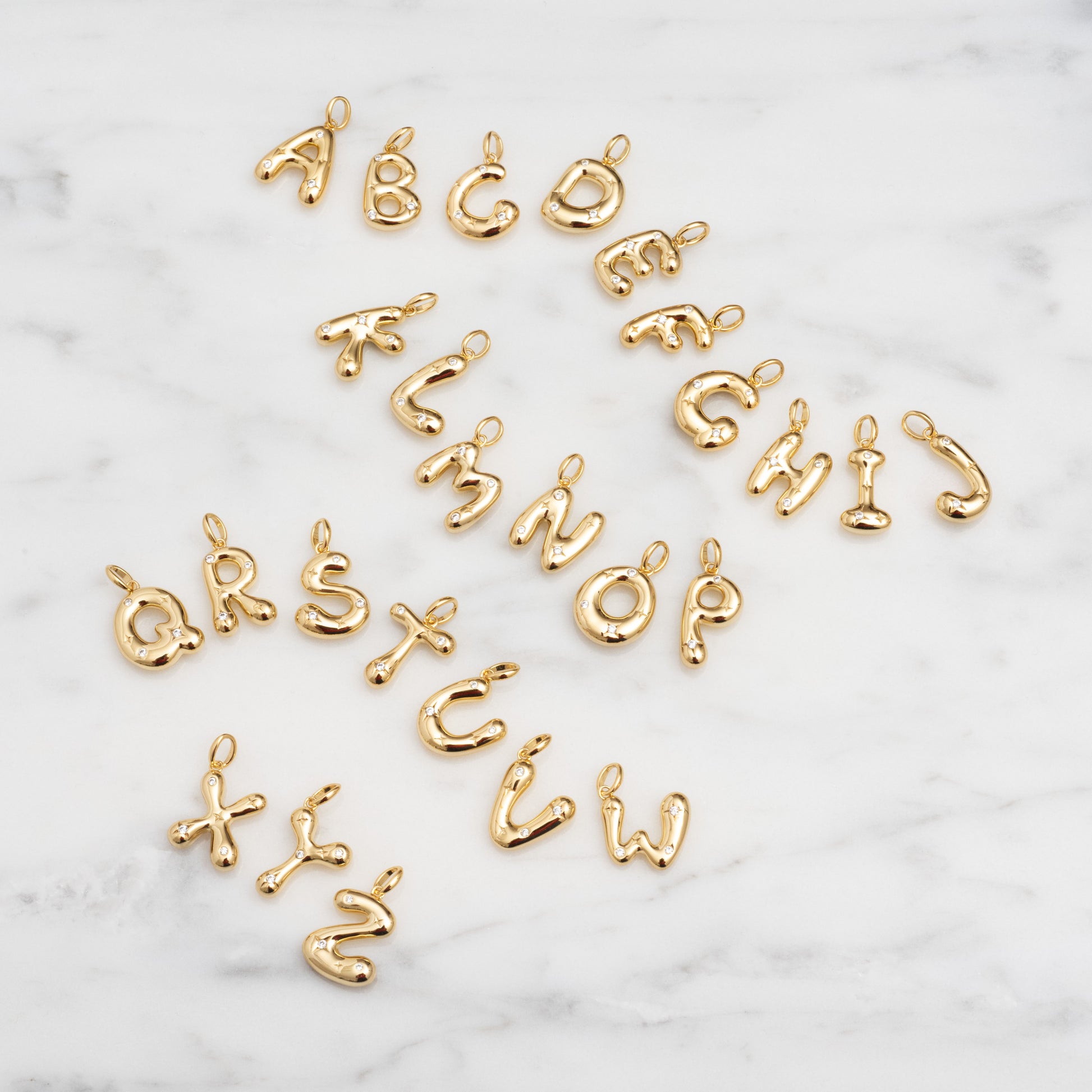 Star Crossed Celestial Bubble Letter Charms arranged on white marble, each charm displays a playful, rounded bubble font featuring letters A to Z.