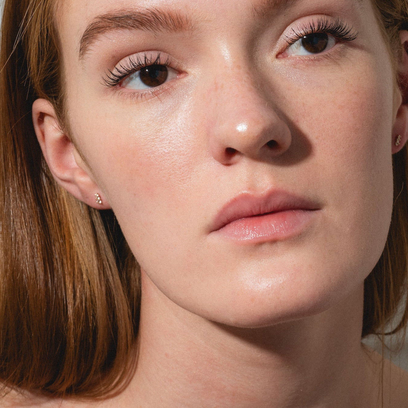 A young woman with fair skin and long auburn hair, wearing a black top, models the Solid Gold Tapered Shimmer Flat Back Studs. She gazes slightly away with a neutral expression against a plain, light background.