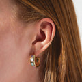 Close-up of a person with straight, reddish-brown hair wearing Opal Ocean Lover Hoops—gold hoop earrings inlaid with rectangular iridescent stones. The softly lit, neutral background highlights the earring's shimmer.