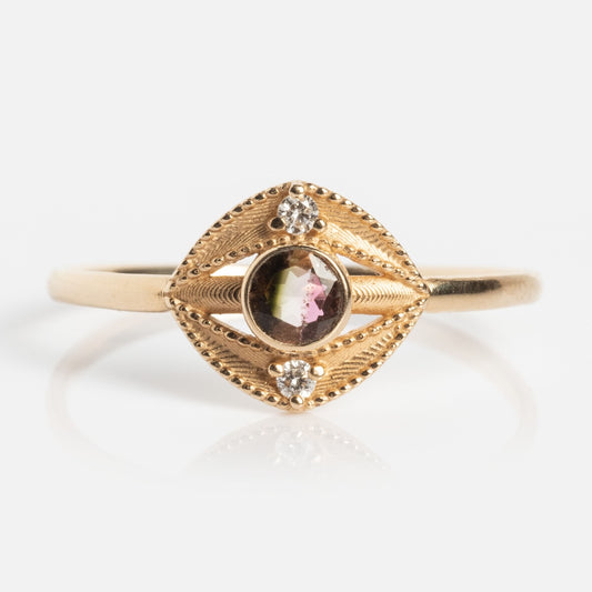 The Staffa White Diamond Ring features a central round gemstone with pink and green hues, set in an eye-shaped gold bezel accented by two white diamonds at the top and bottom, on a plain gold band.