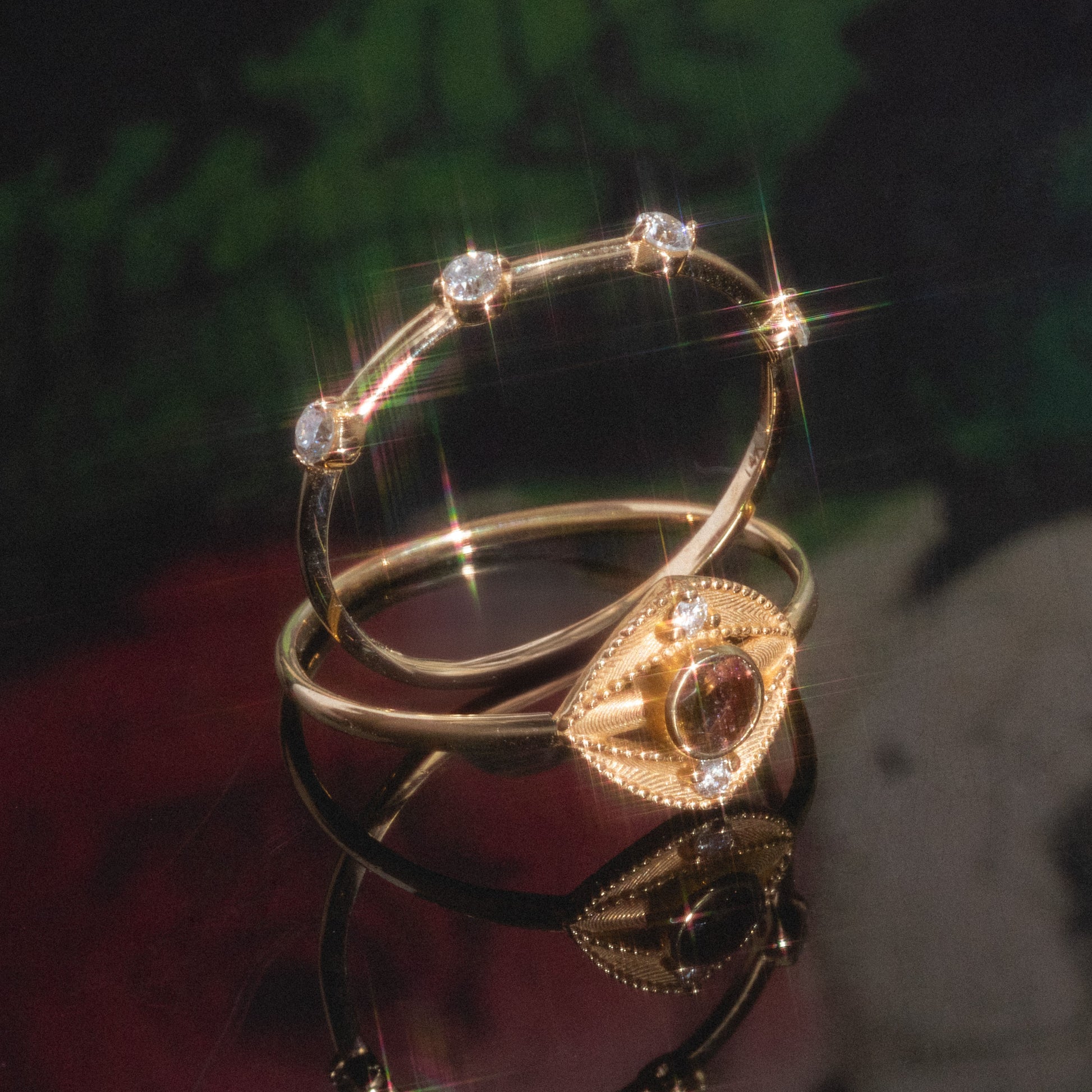 The Munro Ring rests on a reflective surface; it showcases an eye-shaped design with a central gemstone and small diamonds along the band, set against a softly blurred background.