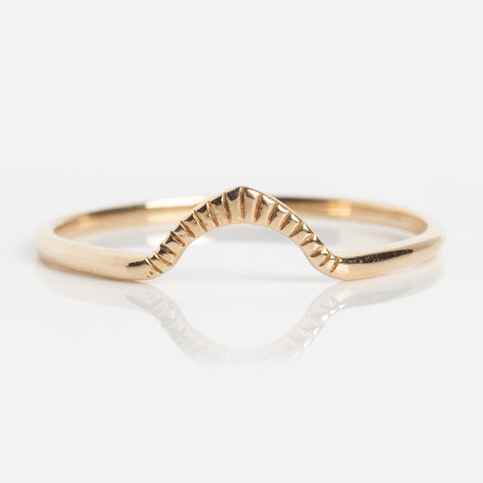 The Cairn Ring is a delicate gold ring featuring a subtle V-shaped curve and textured ridges at its peak, displayed on a plain white background.