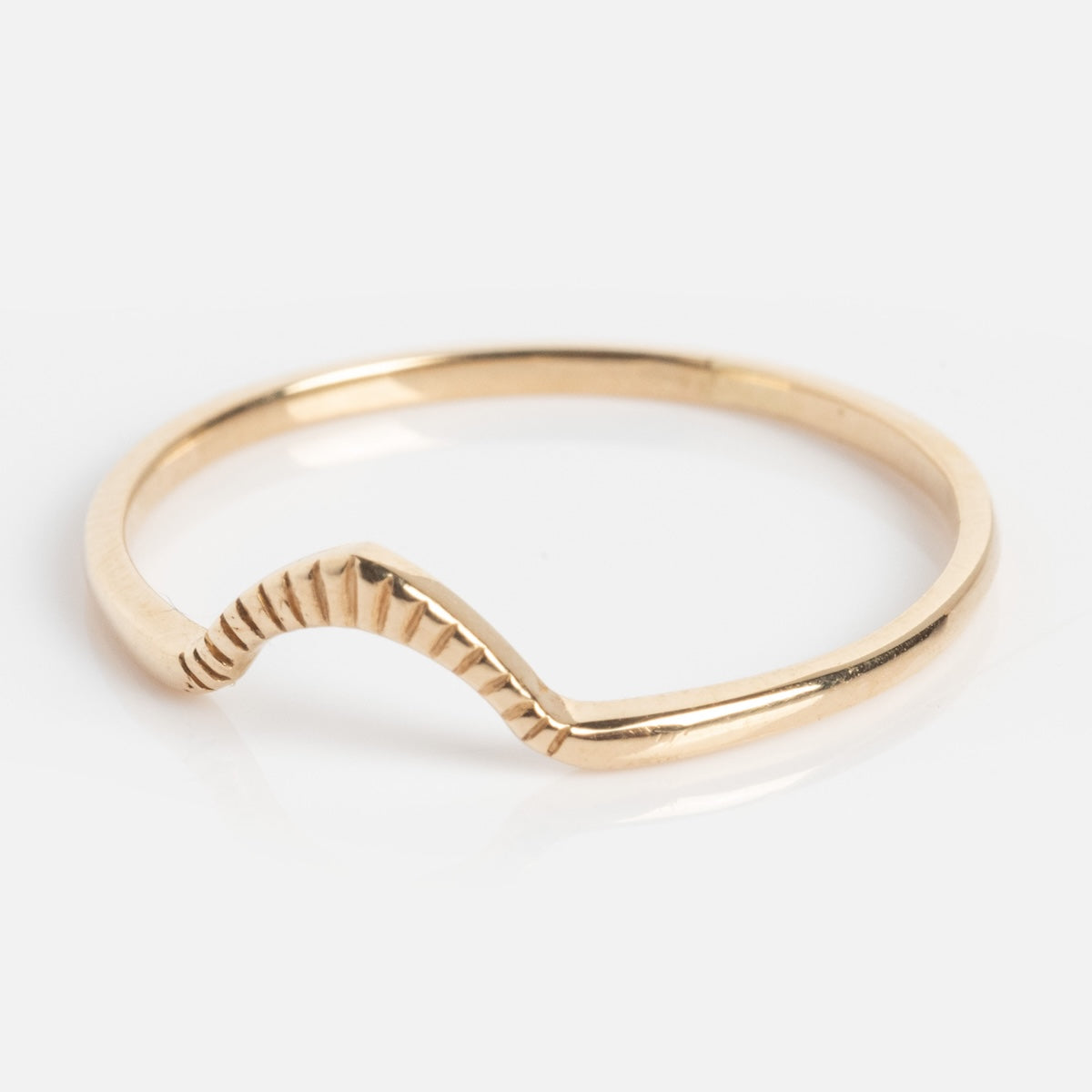 The Cairn Ring is a thin gold band with a subtle V-shaped dip and engraved lines along the inner curve, shown on a plain white background.