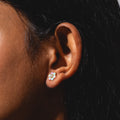 Close-up of a person's ear with straight dark hair, wearing Tropical Opal Fleur Studs—flower-shaped earrings with pastel gemstones—positioned in the earlobe.