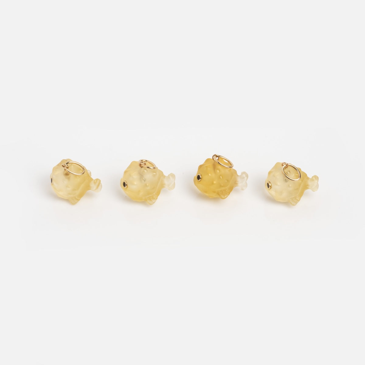 Four Solid Gold Under The Sea Charms, shaped like small fish with metal loops, are neatly arranged on a plain white background—ideal for bringing a nautical accent to your jewelry collection.