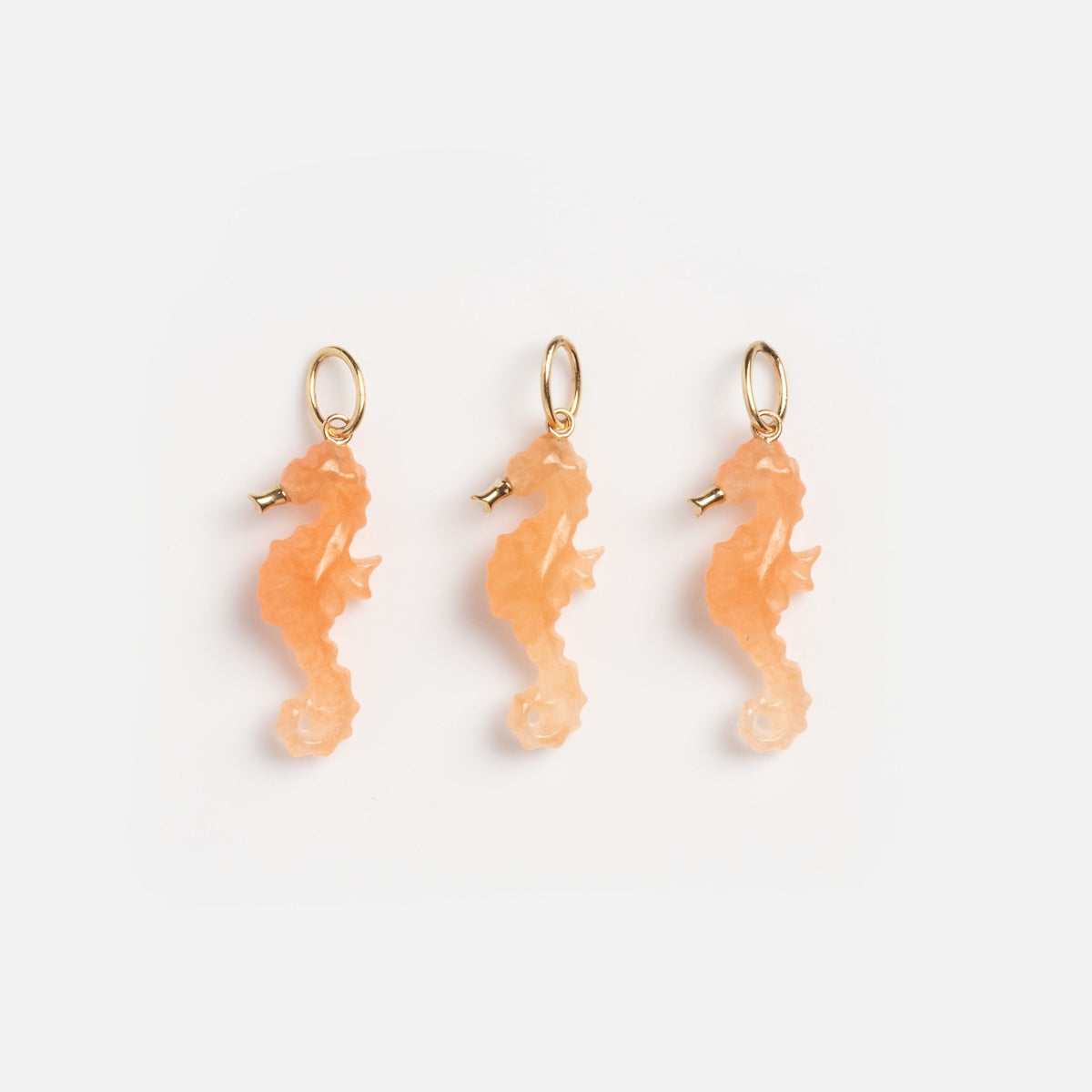 Three Solid Gold Under The Sea Charms, shaped like orange seahorses with gold loops, arranged in a row on a white background—a vibrant accent for any nautical jewelry collection.