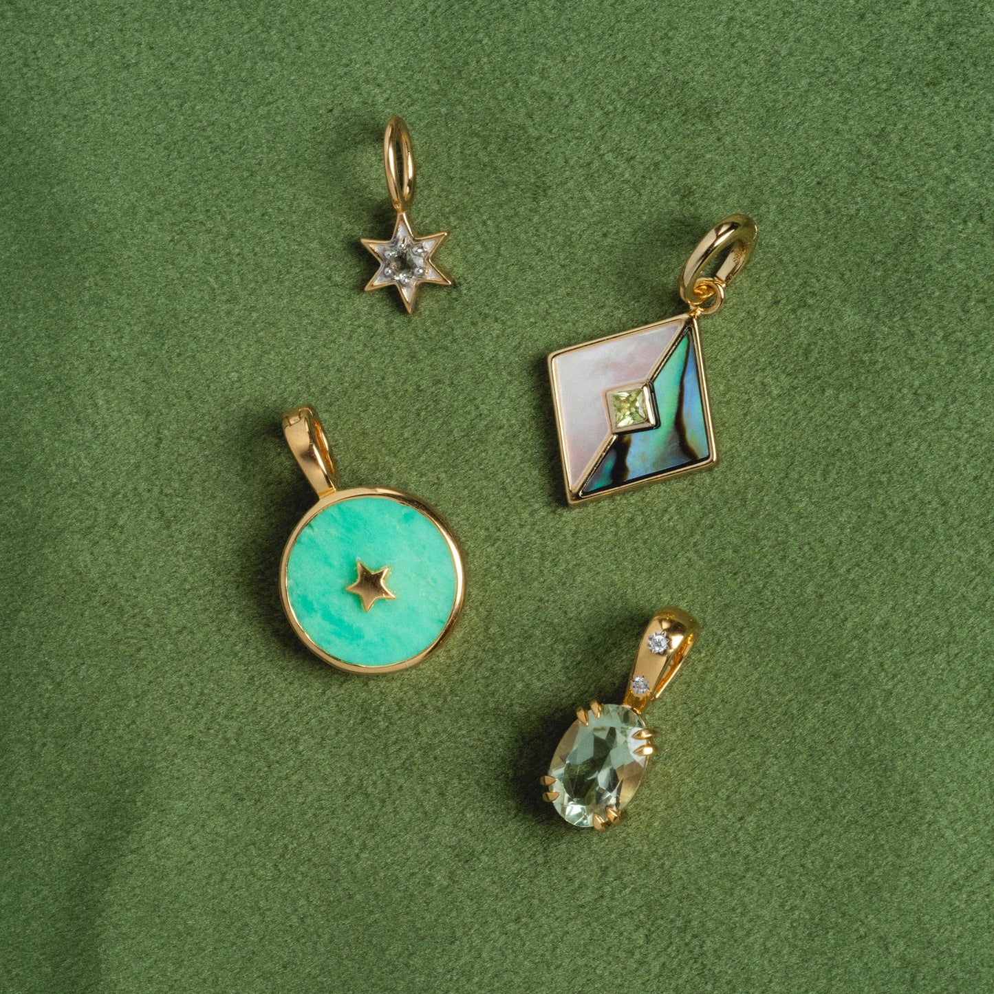 Four statement charms from Charms by Carrie Elizabeth Jewelry rest on a green textured surface: a crystal star, colorful square, round turquoise with star cutout, and oval gemstone—all in 14k gold vermeil.