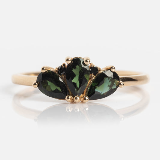 The Ava Black Diamond Ring is a 14k solid gold ring with three pear-shaped black diamonds set side by side in a fan-like design, accented by small gold prongs on a simple band.