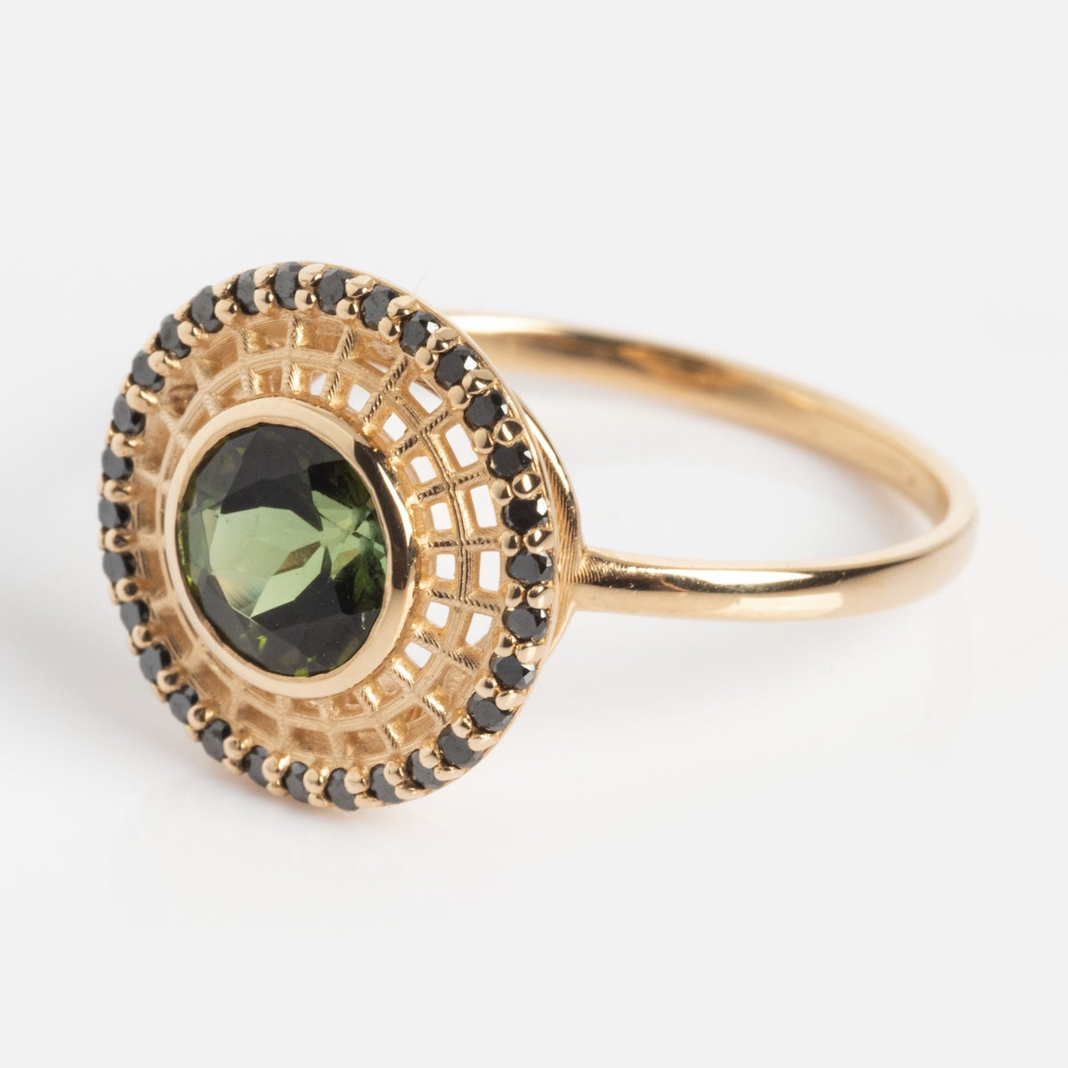 The Tantallon Black Diamond Ring features a gold band with an ornate circular setting, showcasing a central green gemstone encircled by small black stones.