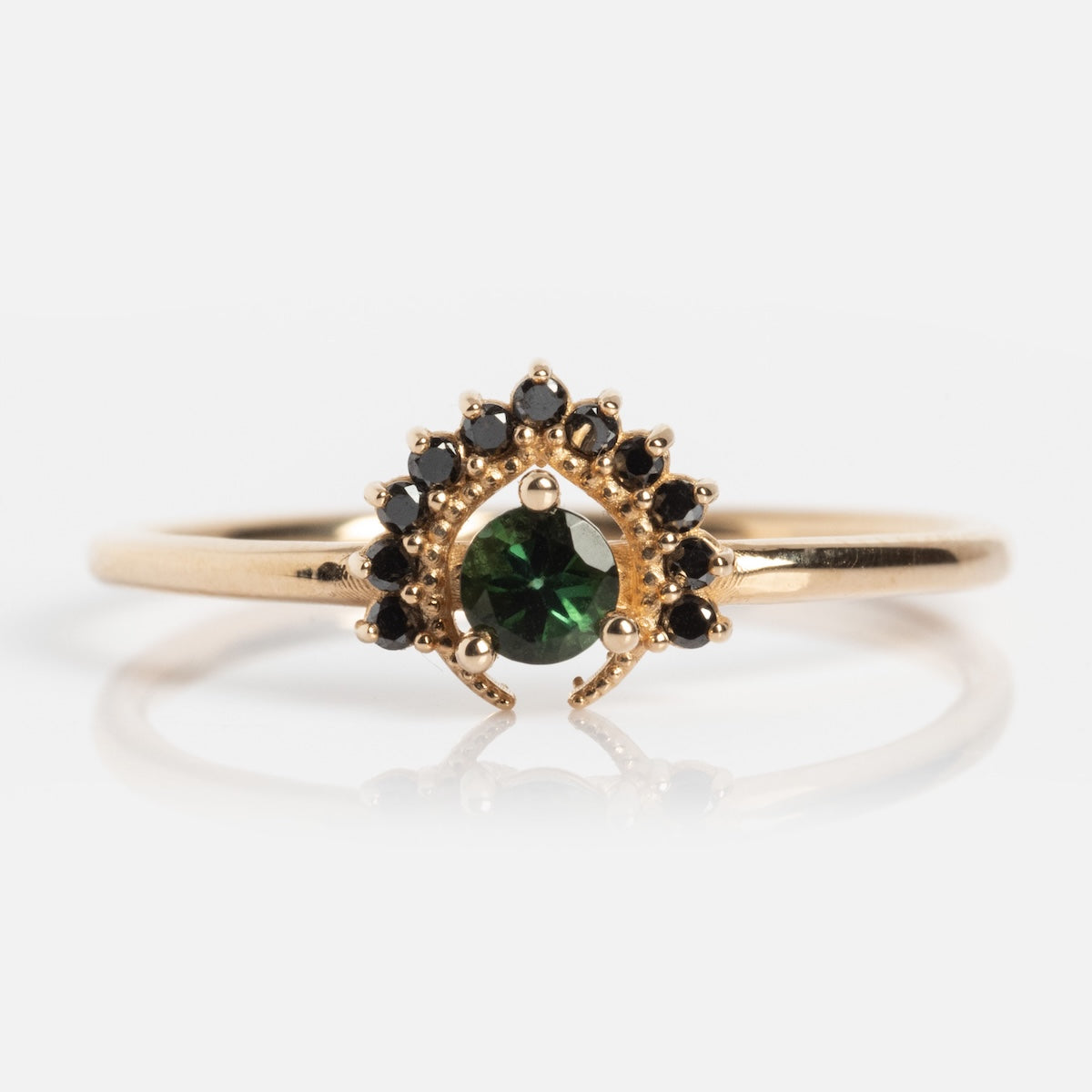 The Tosia Tourmaline Ring features a central round bi-color tourmaline set in solid gold, accented by a fan-shaped semicircle of small black diamonds.