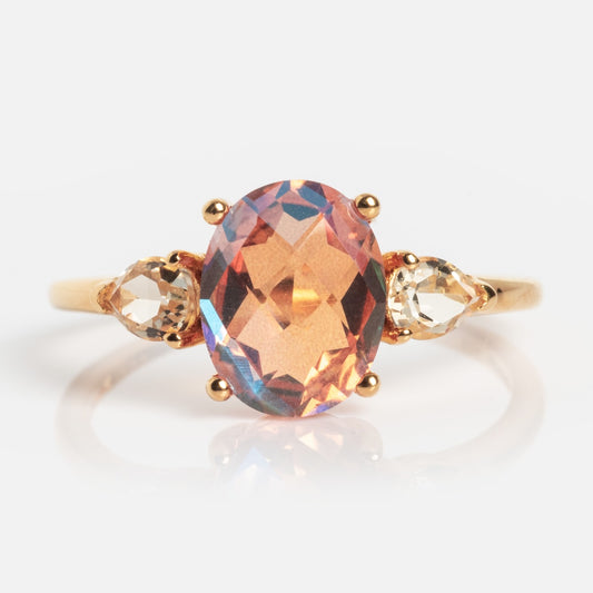 The Pippa Quartz Ring is a gold ring with a large, oval-cut peach quartz center stone and two smaller, clear pear-shaped stones on each side, displayed on a plain white background.