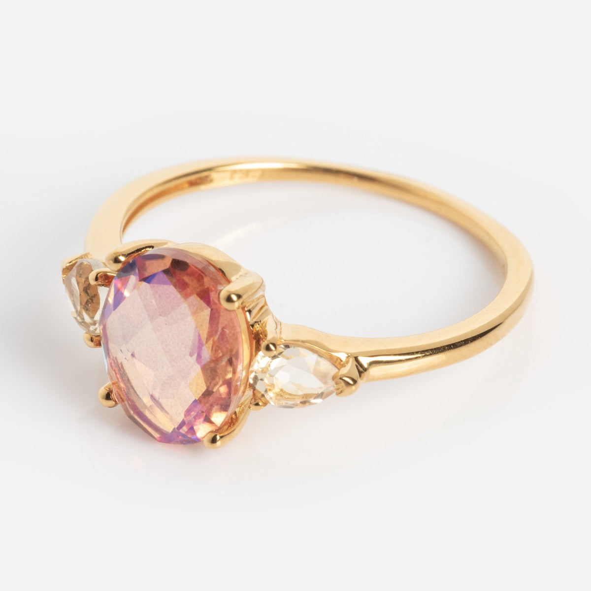The Pippa Quartz Ring is a gold ring with a large oval pink quartz centerpiece, flanked by two smaller clear stones, set against a plain white background.