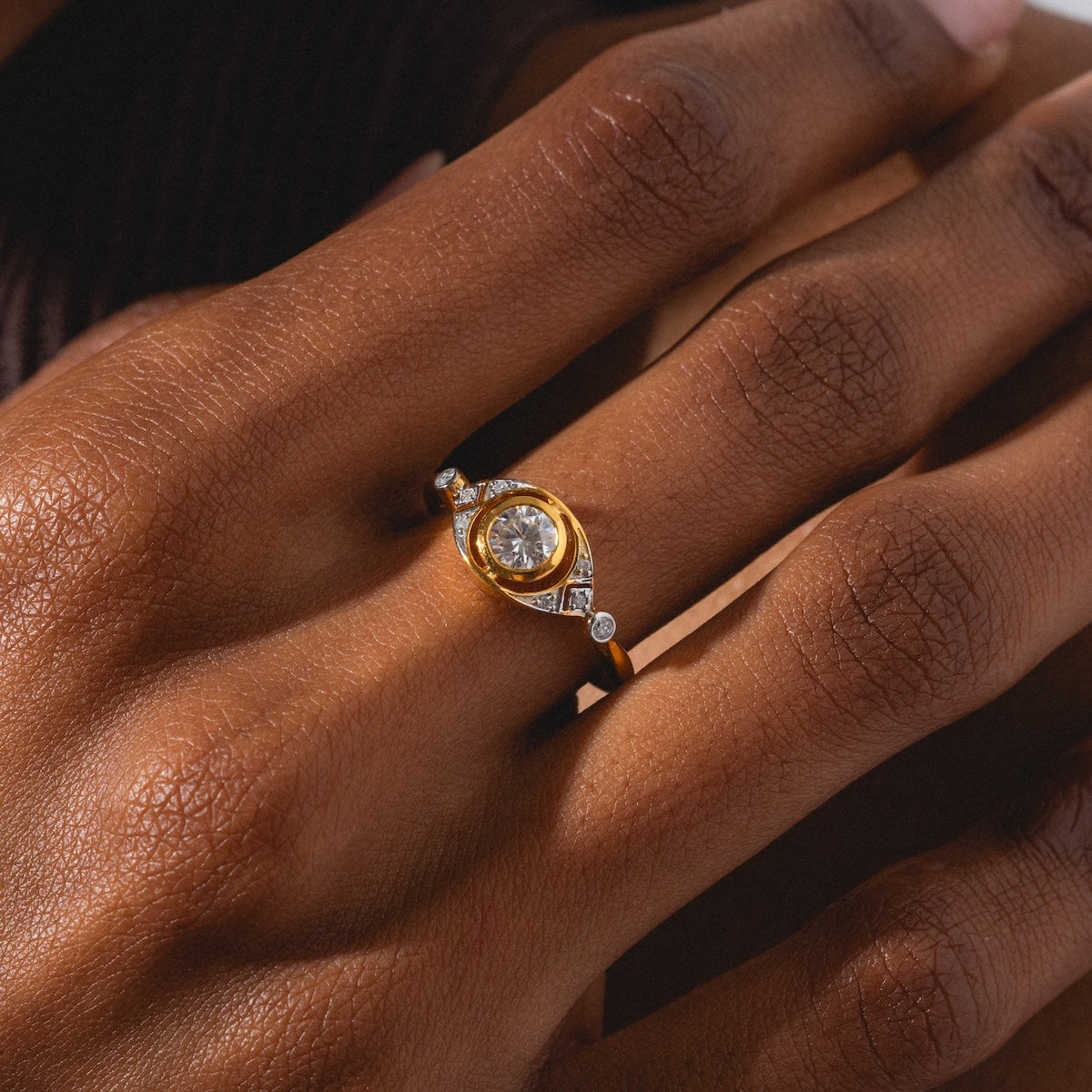 A close-up of a hand wearing the Vienna Moissanite and Diamond Ring, featuring a large central moissanite flanked by smaller diamonds, set against a softly lit background.