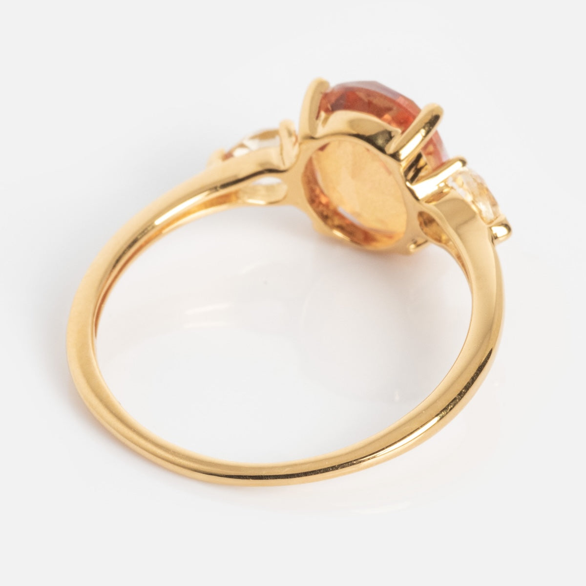 The Pippa Quartz Ring, a gold band with a prominent oval orange gemstone at the center and two smaller clear stones on each side, is displayed from an angled side view against a white background.