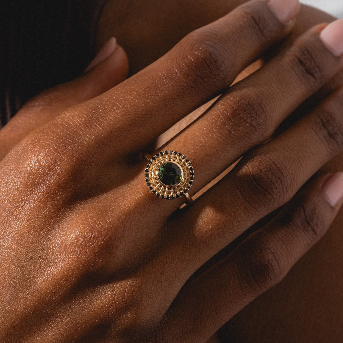 A close-up of a hand with manicured nails wearing the Tantallon Black Diamond Ring, which features a large dark green gemstone encircled by smaller stones in a circular pattern.