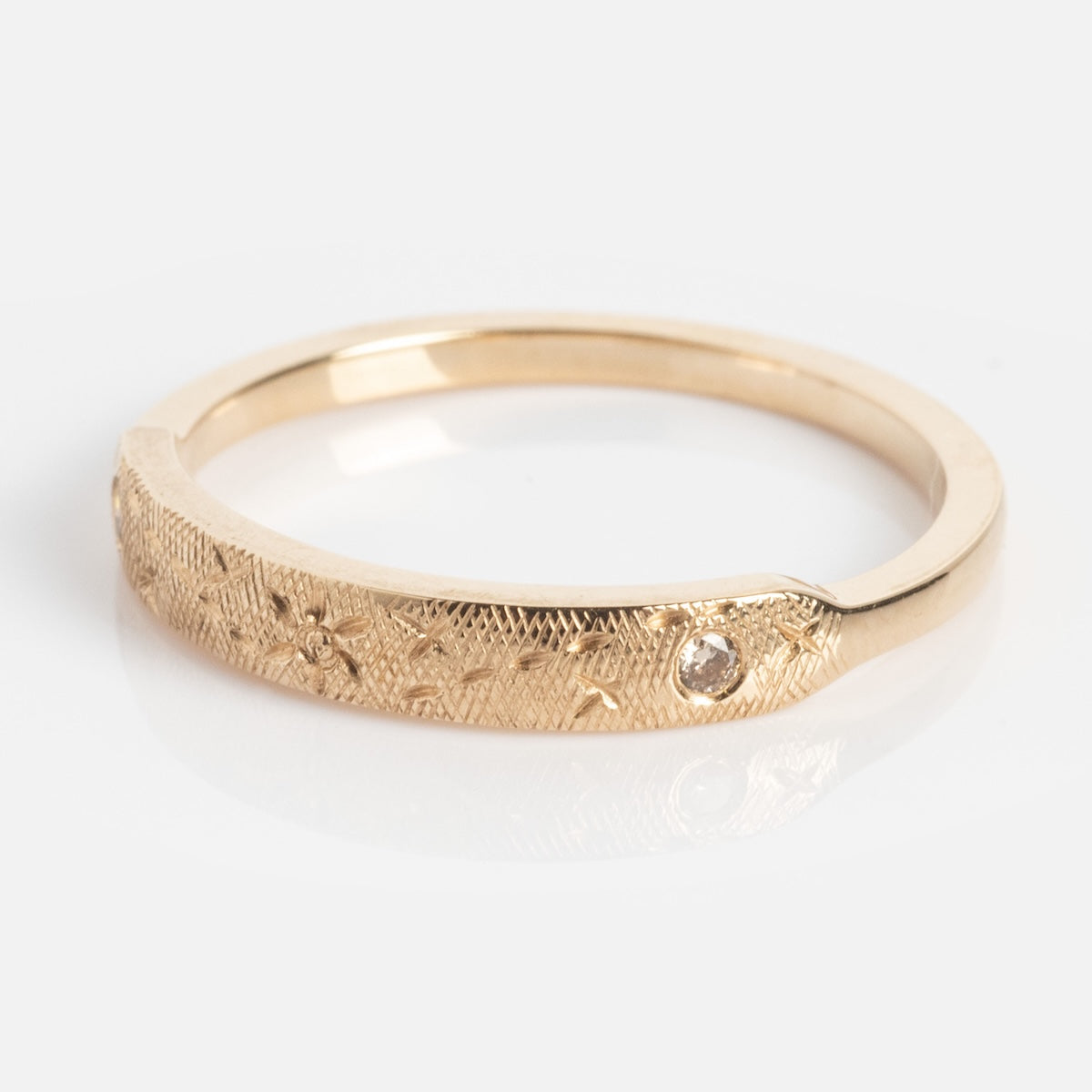 The Dukes Champagne Diamond Ring features a delicate gold band with an engraved, textured design and a small round diamond set in the surface, shown on a white background.