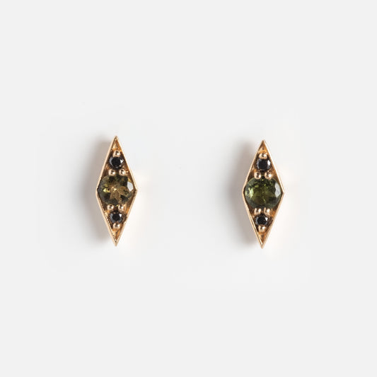 The Shillay Studs are gold, diamond-shaped earrings featuring green center stones and small black accents, shown on a plain white background.