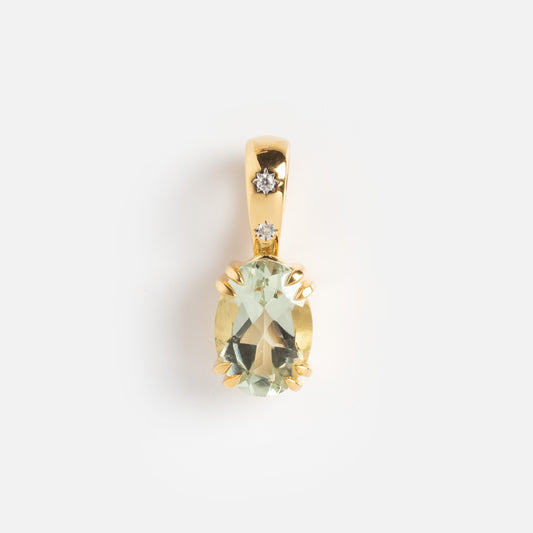 The Charms pendant by Carrie Elizabeth Jewelry features an oval pale green gemstone held by four prongs, topped with two small round white stones on the gold bail, all displayed against a plain white background.