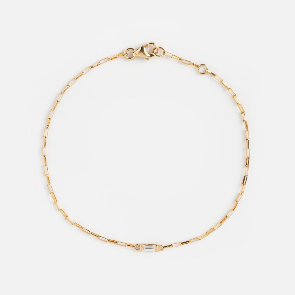 The Sunblink Diamond Bracelet is a delicate gold chain with rectangular links, featuring a small baguette-cut clear stone at the center and secured by a lobster clasp.